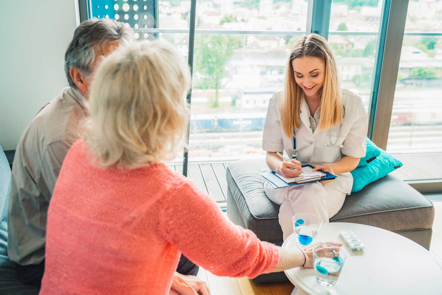 A healthcare professional taking notes while consulting with elderly patients in a bright, modern office.